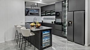 Una cocina moderna con una isla central, taburetes de bar, un enfriador de vino integrado y un refrigerador.