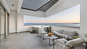 Un balcón moderno con vistas al mar, una zona de estar con cojines y una mesita con frutero.