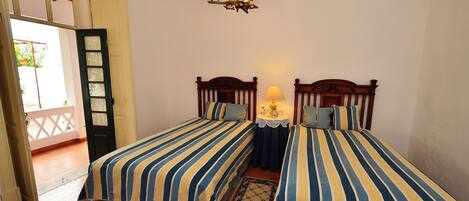 A room with two beds, a chandelier, a small table with a lamp, and a patterned rug.