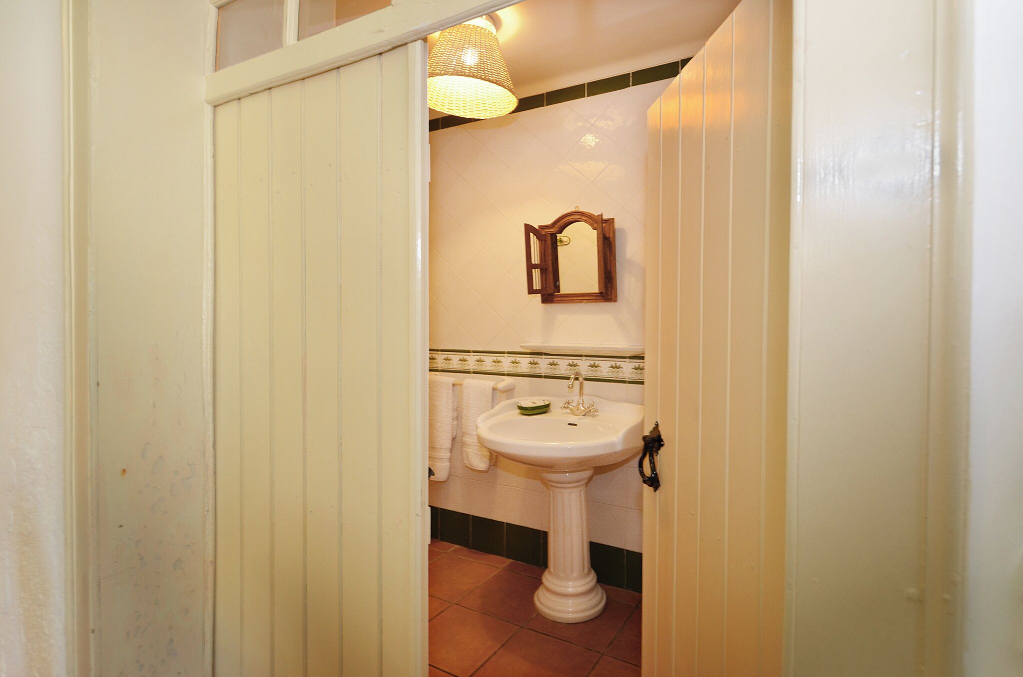 A bathroom with a white pedestal sink, a mirror, and a towel hanging on the wall.