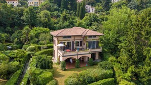 Une grande maison à deux étages, entourée d’une végétation luxuriante et de collines.