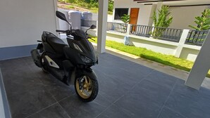 A scooter parked in a covered outdoor area with a tiled floor.