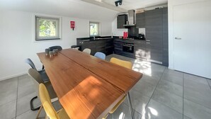 A modern kitchen with dark cabinetry, a wooden dining table, and a fire extinguisher on the wall.