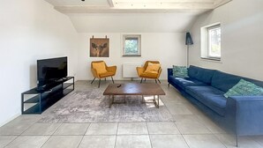 A modern living room with a TV, two yellow armchairs, a blue sofa, and a coffee table.