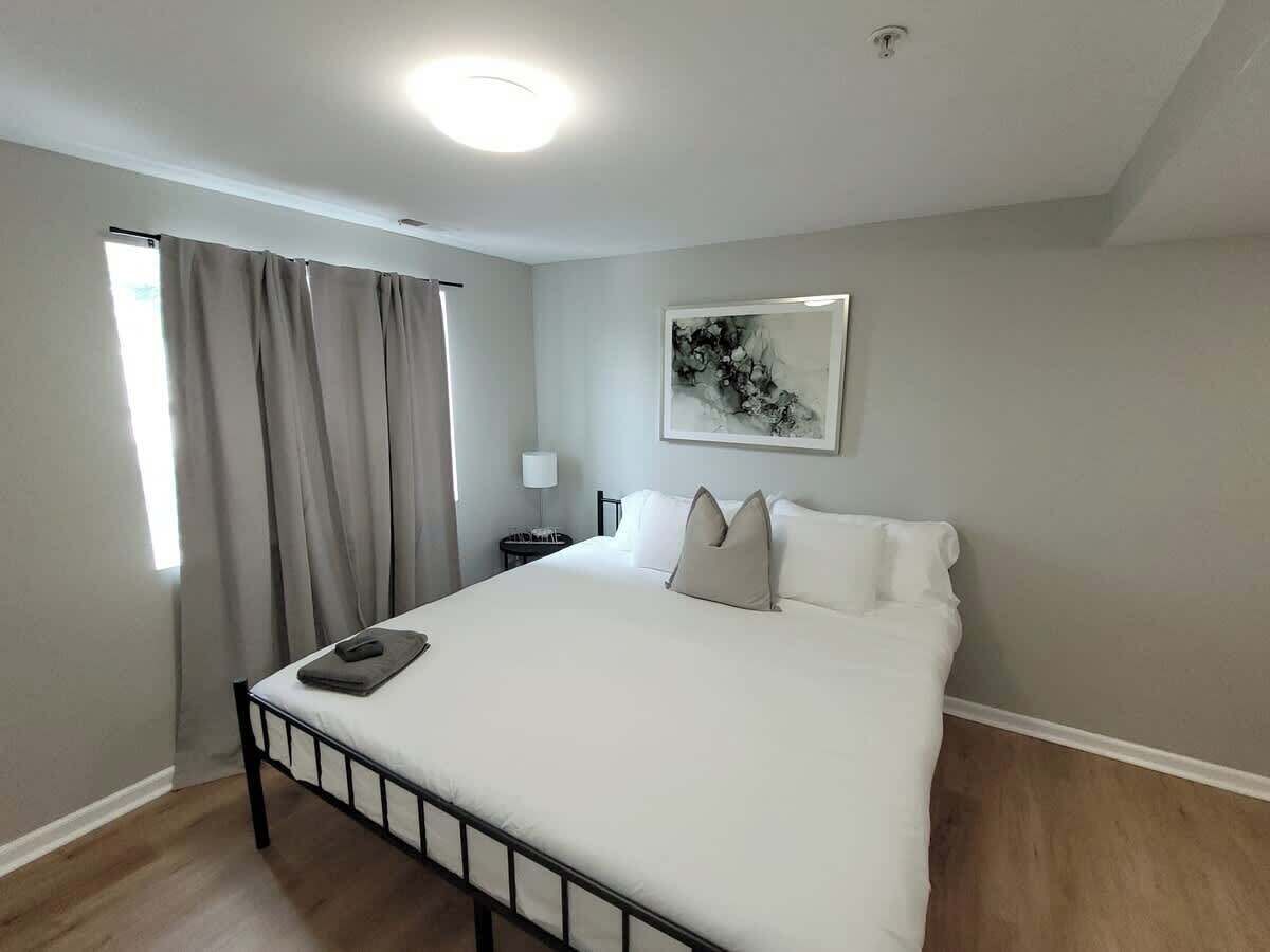 A bedroom with a large bed, a bedside table, a lamp, and a window with curtains.