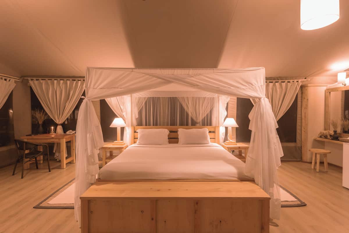 A four-poster canopy bed with a wooden headboard, bedside tables with lamps, and a small desk with a chair.
