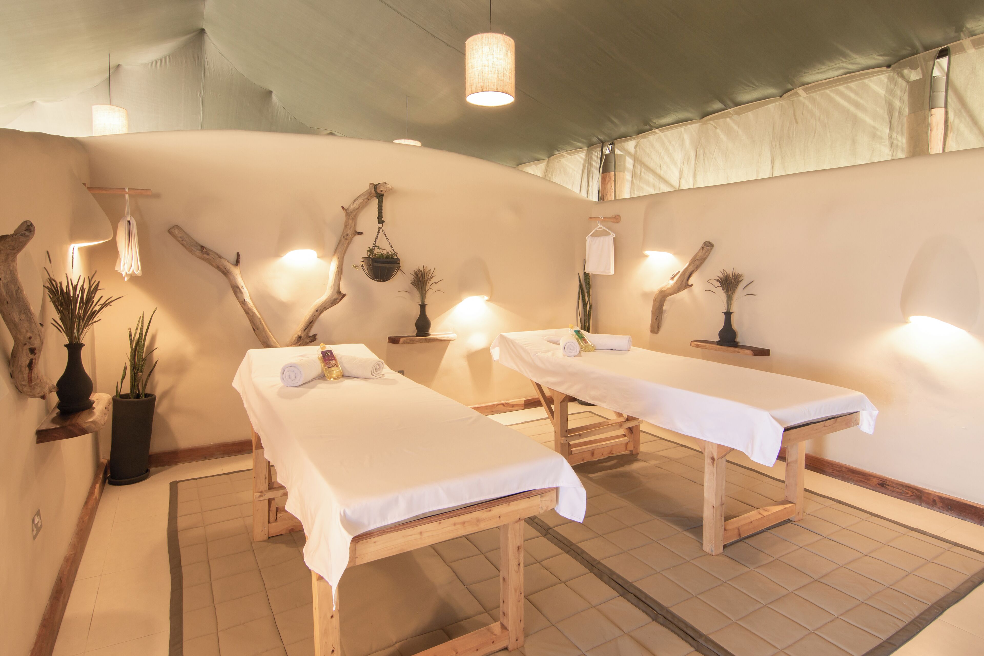 A spa room with two wooden massage tables, potted plants, and hanging lights.