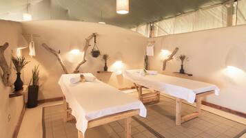 A spa room with two wooden massage tables, potted plants, and hanging lights.