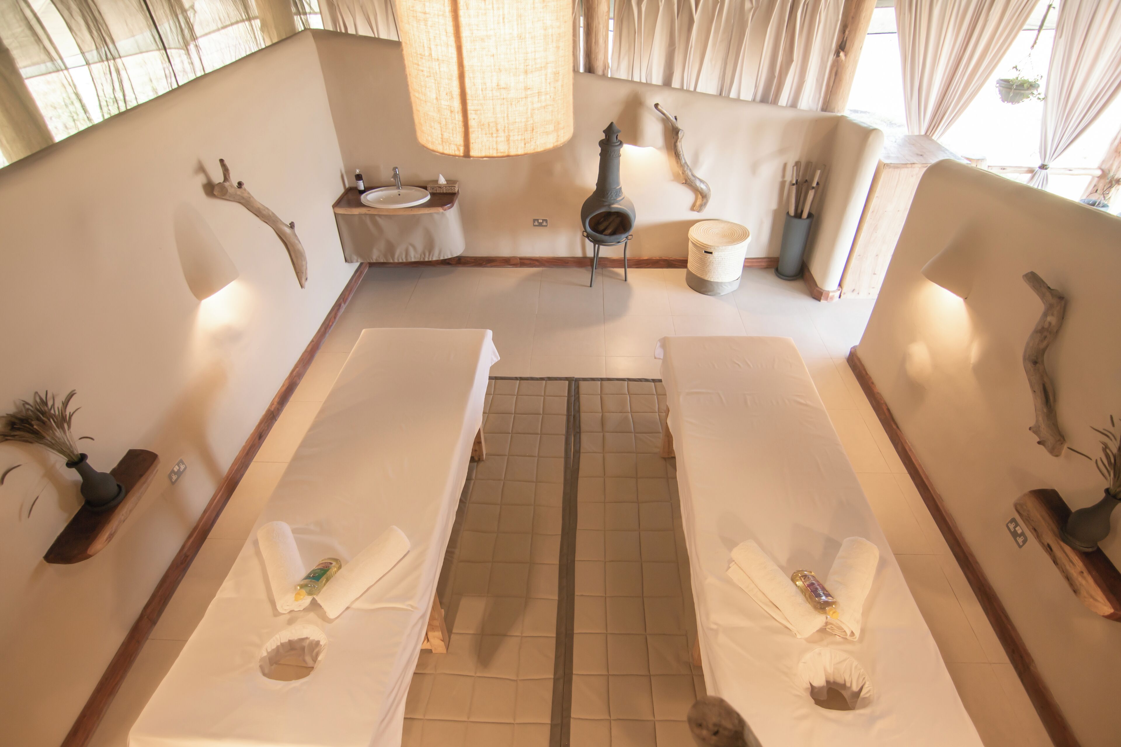 A spa room with two massage tables, a sink, and a decorative wall.