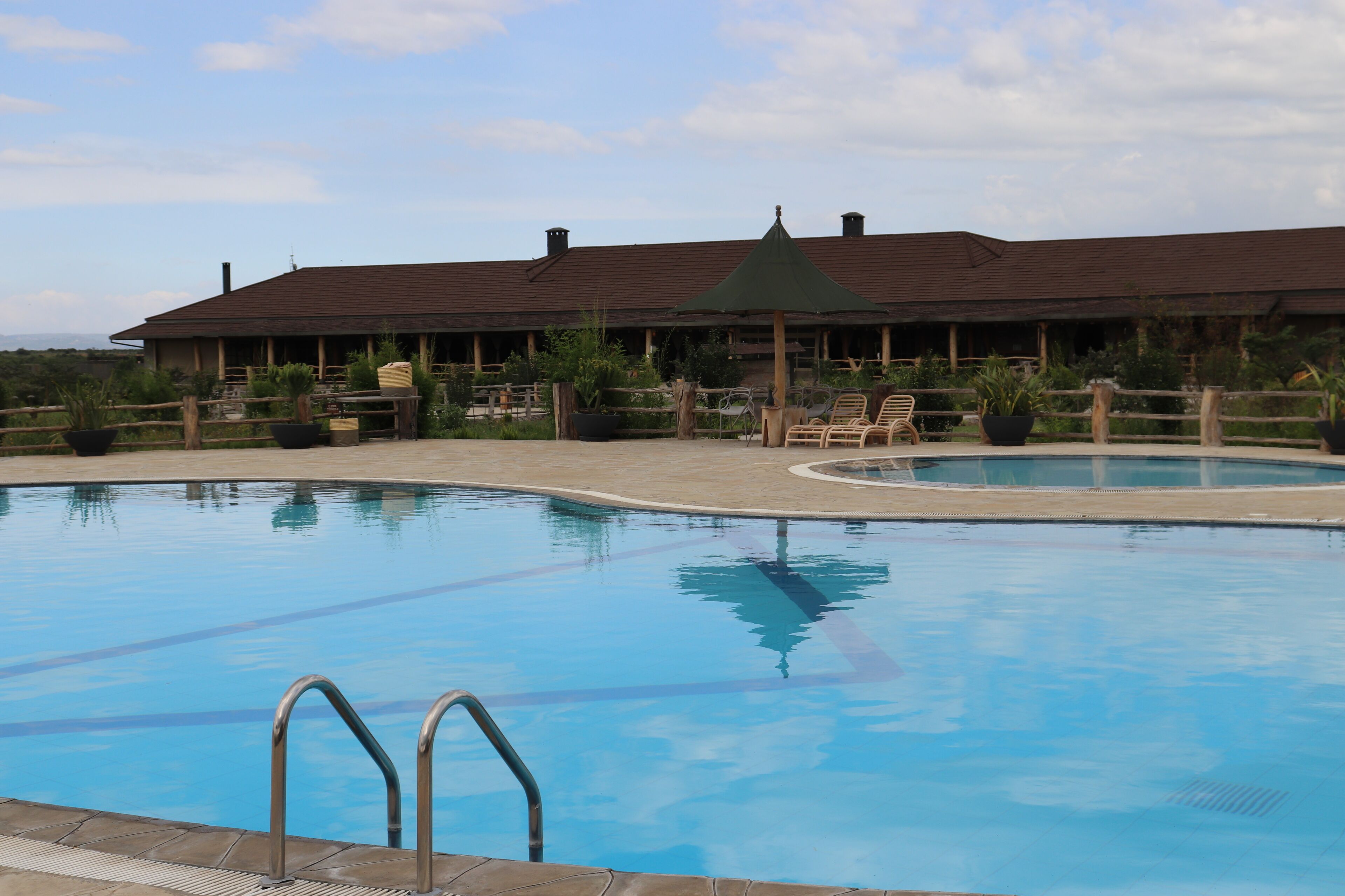 Une piscine avec une terrasse en bois, des chaises longues et un espace salon abrité.