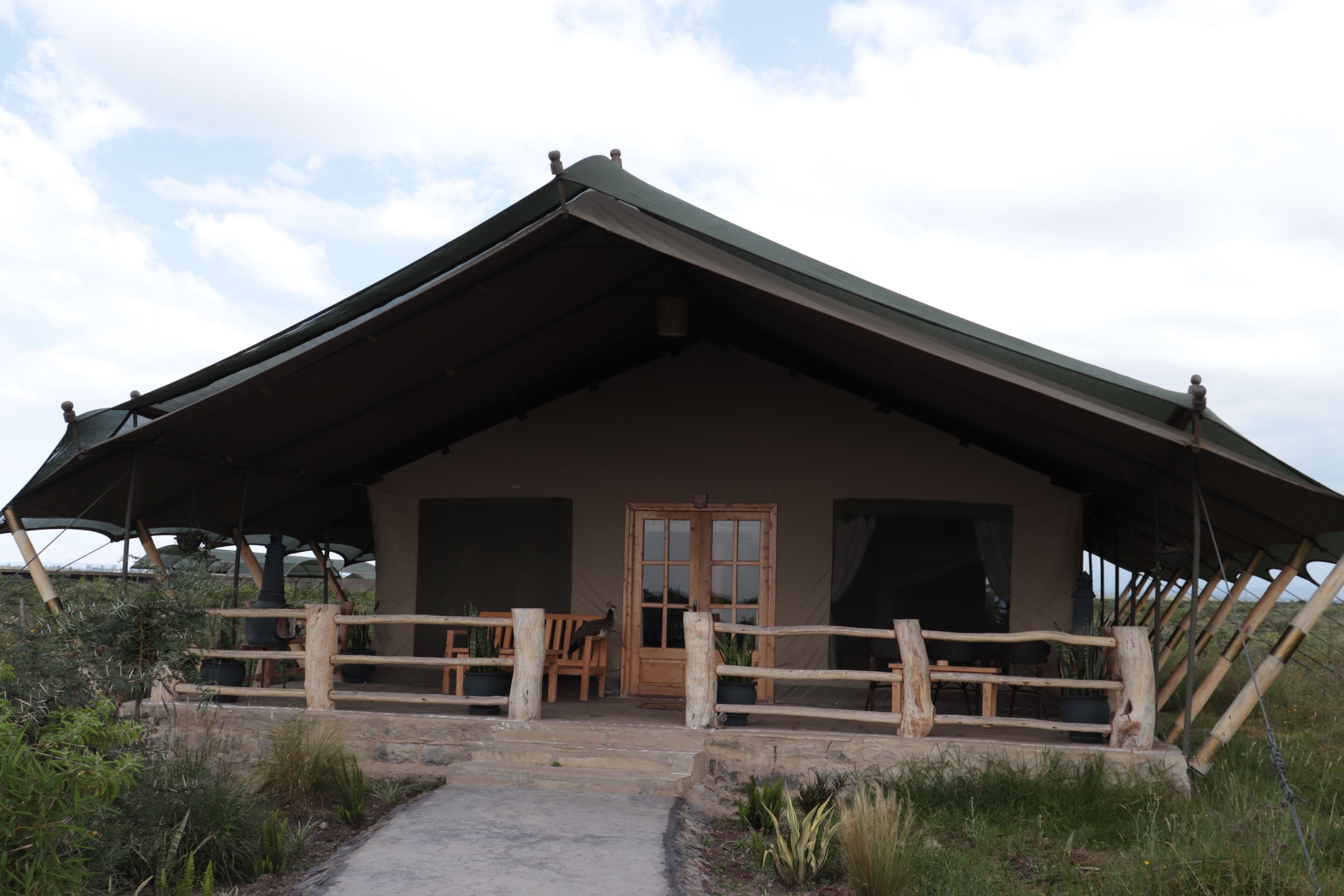 A rustic lodge with a large porch, wooden fence, and a door leading to the interior.