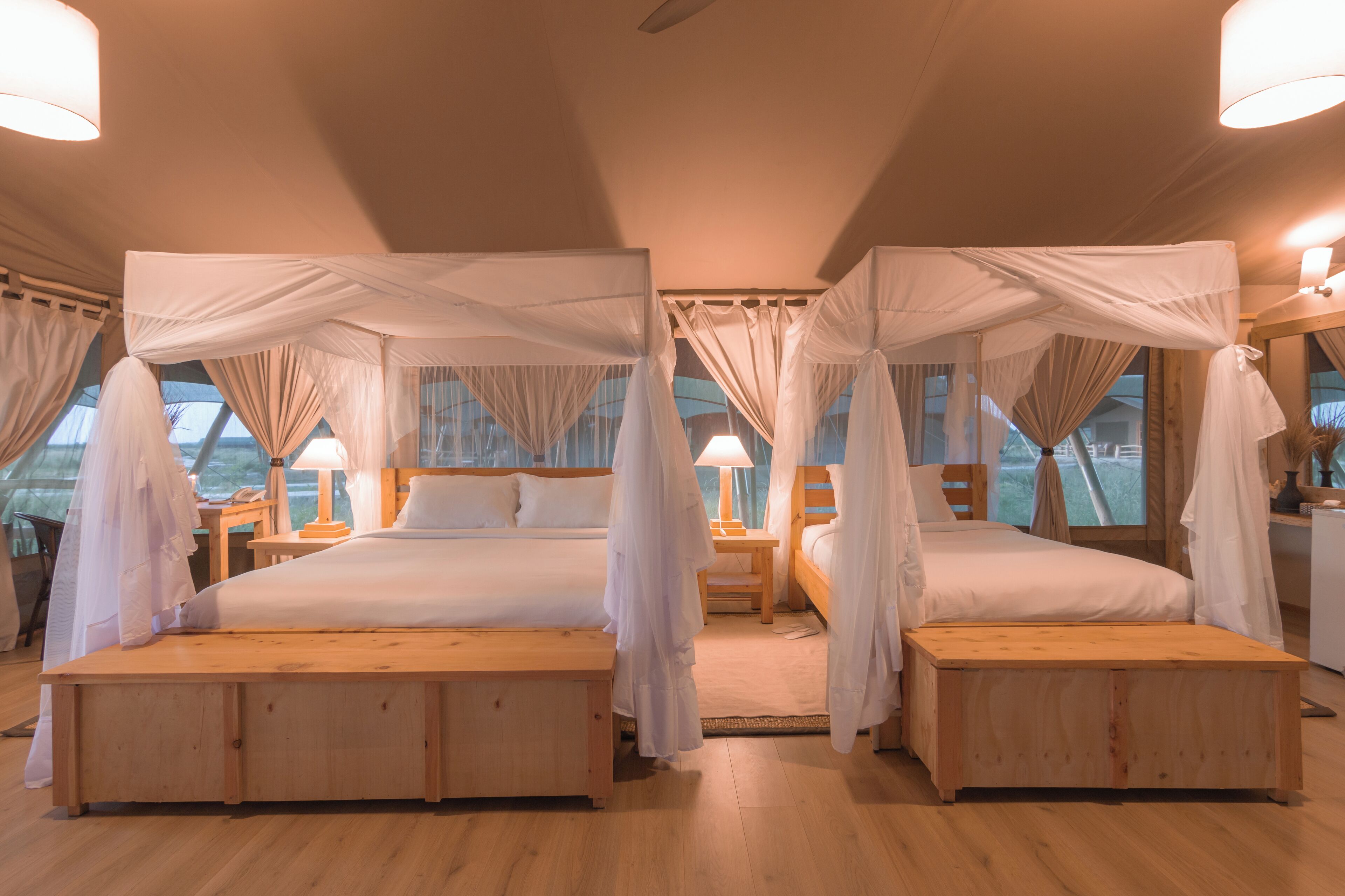 A room with two beds, each with a canopy, wooden headboards, bedside tables, and lamps.