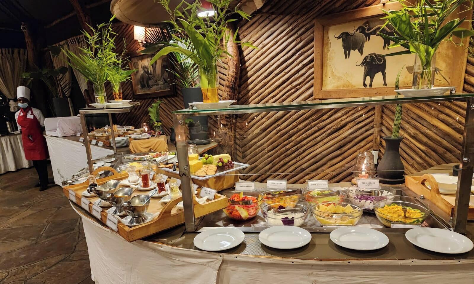 A buffet setup with various food items and a staff member in uniform.