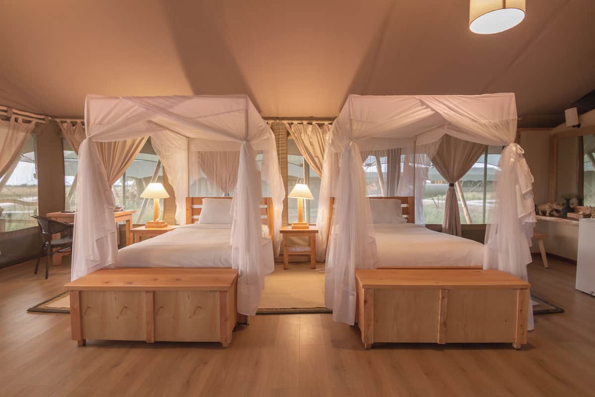 A room with two beds, each with a canopy, wooden headboards, bedside tables, and lamps.