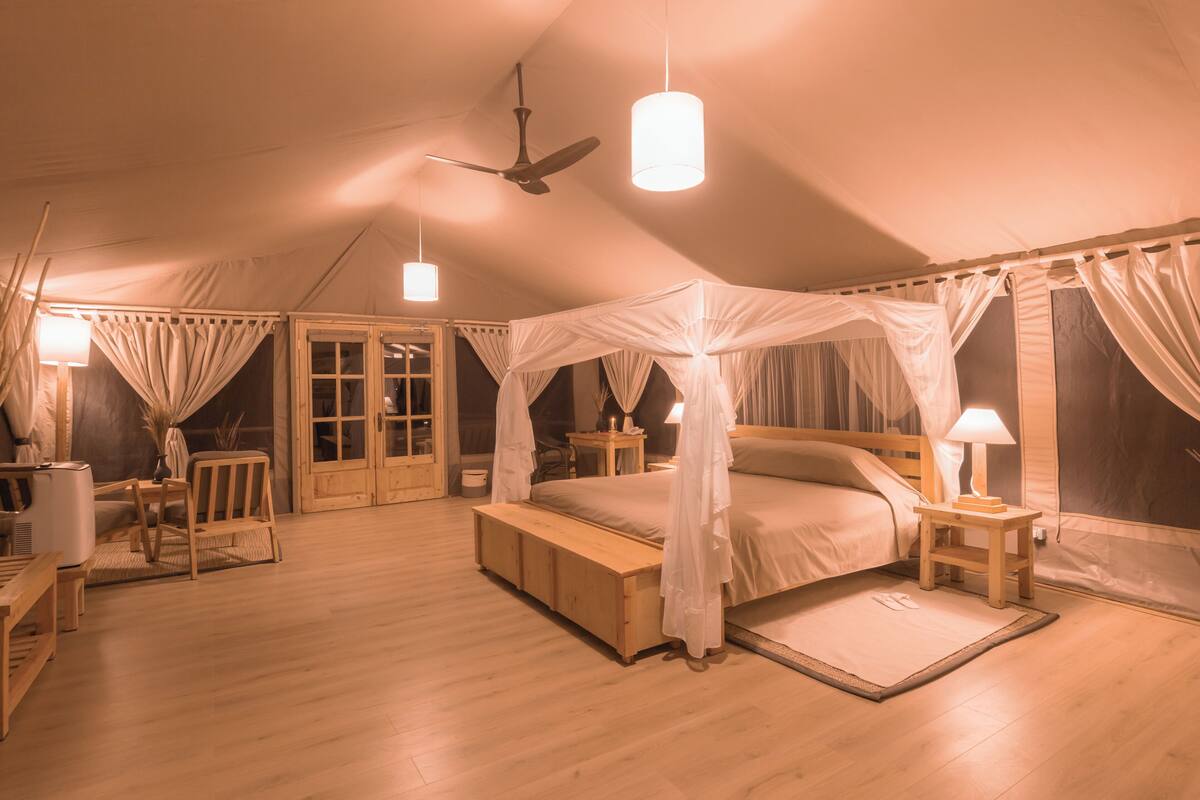 A tent-style bedroom with a canopy bed, wooden furniture, and a ceiling fan.