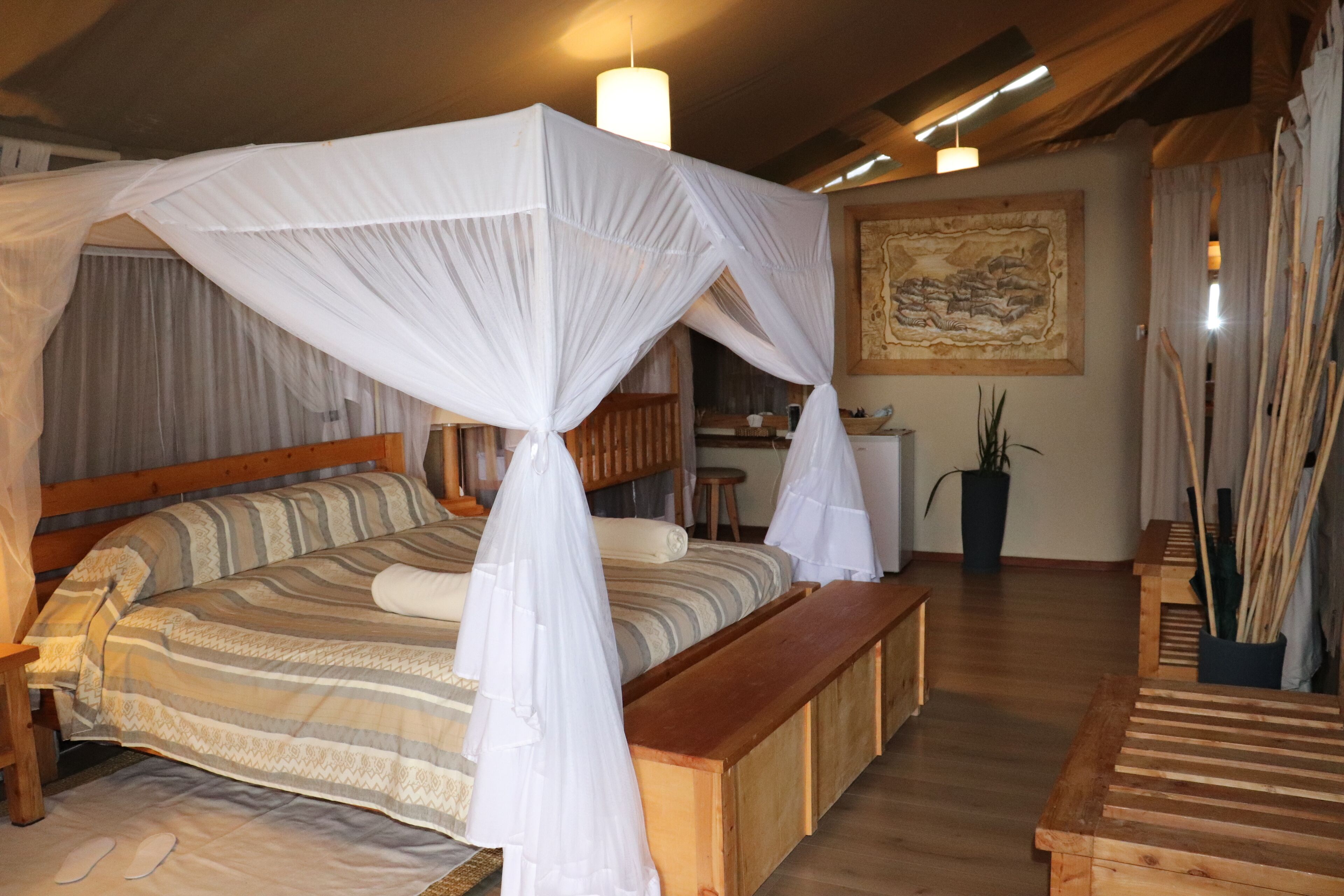 A bedroom with a four-poster bed, wooden headboard, bedside tables, a bench, and a large painting on the wall.