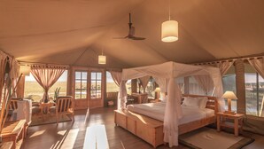 Une chambre aménagée comme une tente, avec un lit, des tables de chevet et une vue sur l’extérieur.