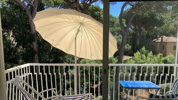 Un balcon avec une balustrade blanche, un parasol beige et deux chaises dotées de coussins à rayures.