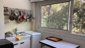 Une cuisine compacte avec une fenêtre, un évier, une cuisinière et un égouttoir contenant des casseroles et des poêles.