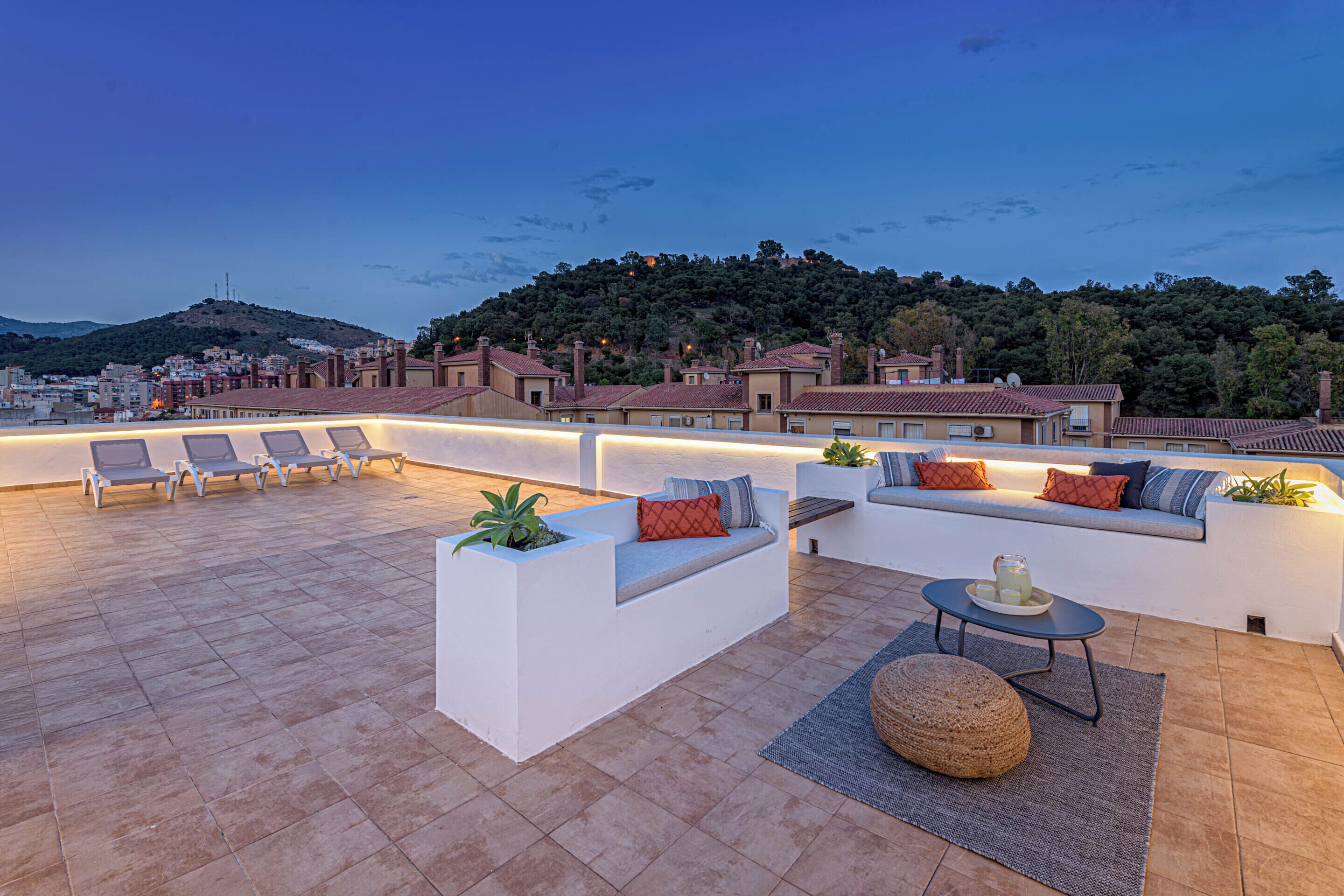Una terraza en la azotea con mobiliario exterior, una pequeña mesa y vistas a un pueblo en la colina.