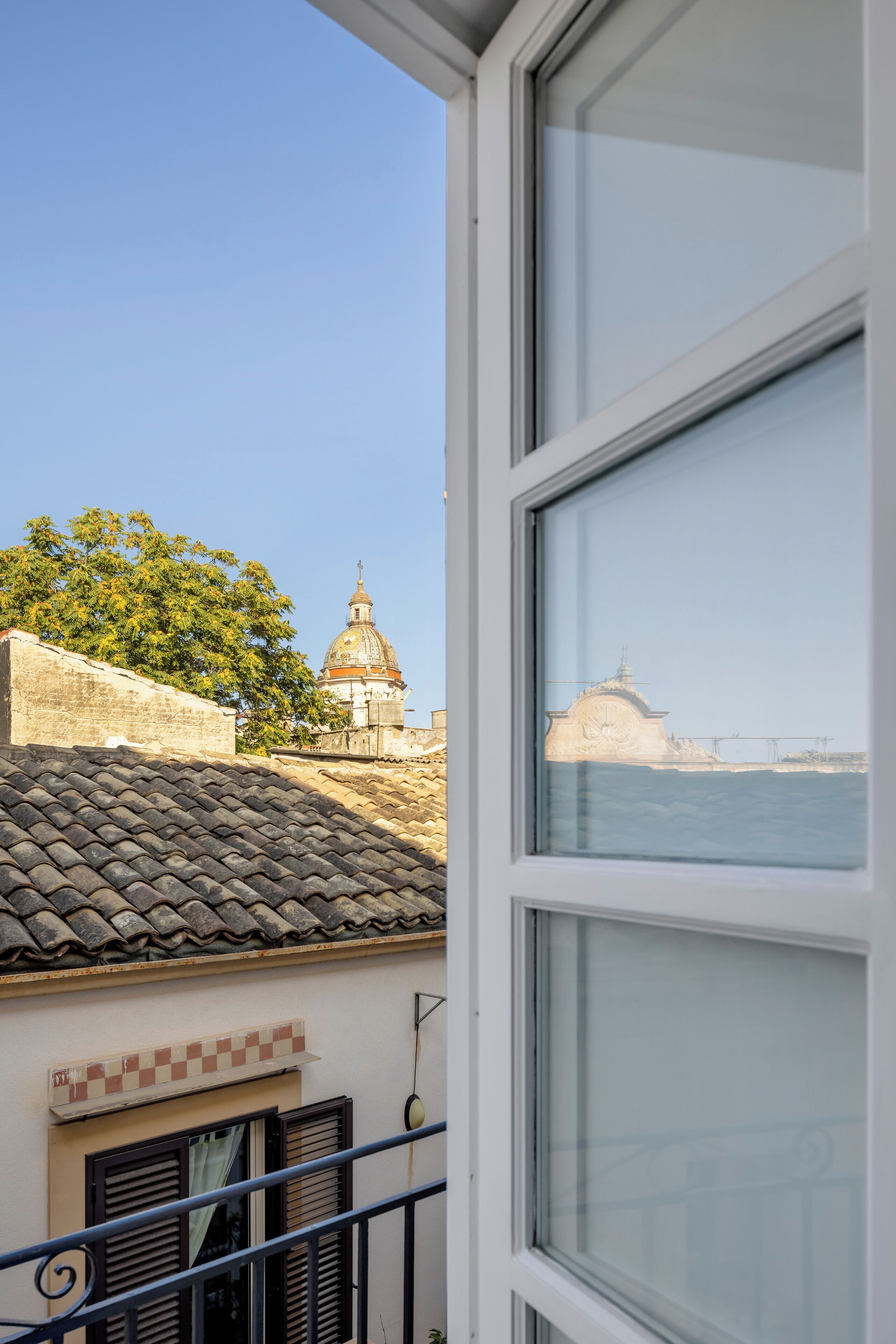 A view from a balcony with a tiled roof, a window, and a building with a dome and a clock tower in the background.