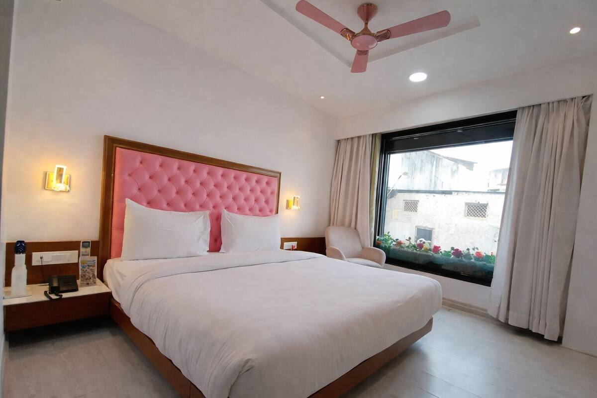 A hotel room with a large bed, a ceiling fan, a nightstand with a phone, and a window with curtains.