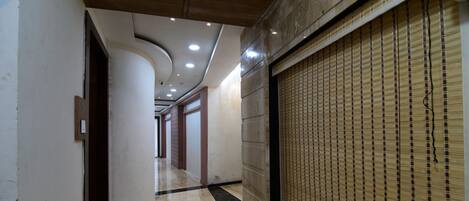 A corridor with a polished floor, a curved ceiling with recessed lighting, and a wall with a patterned blind.
