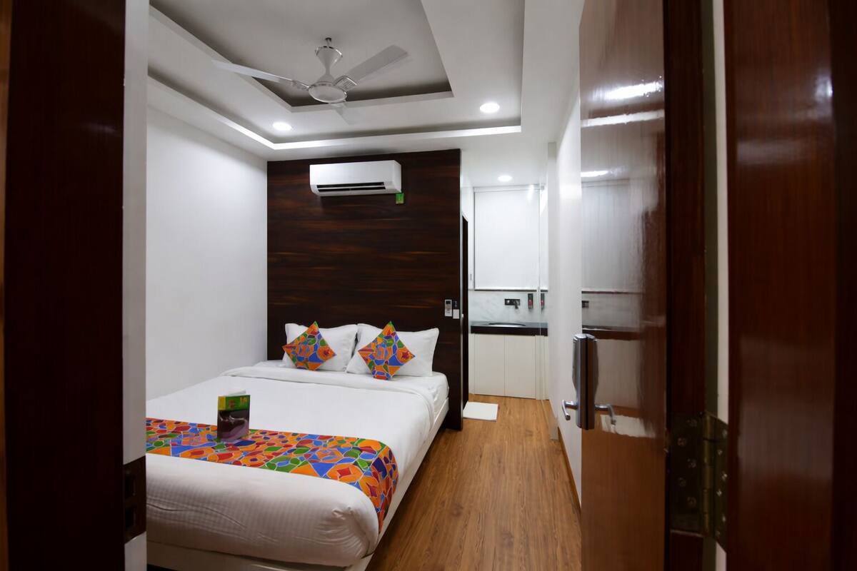 A compact hotel room with a bed, a ceiling fan, a small kitchenette, and a wooden floor.