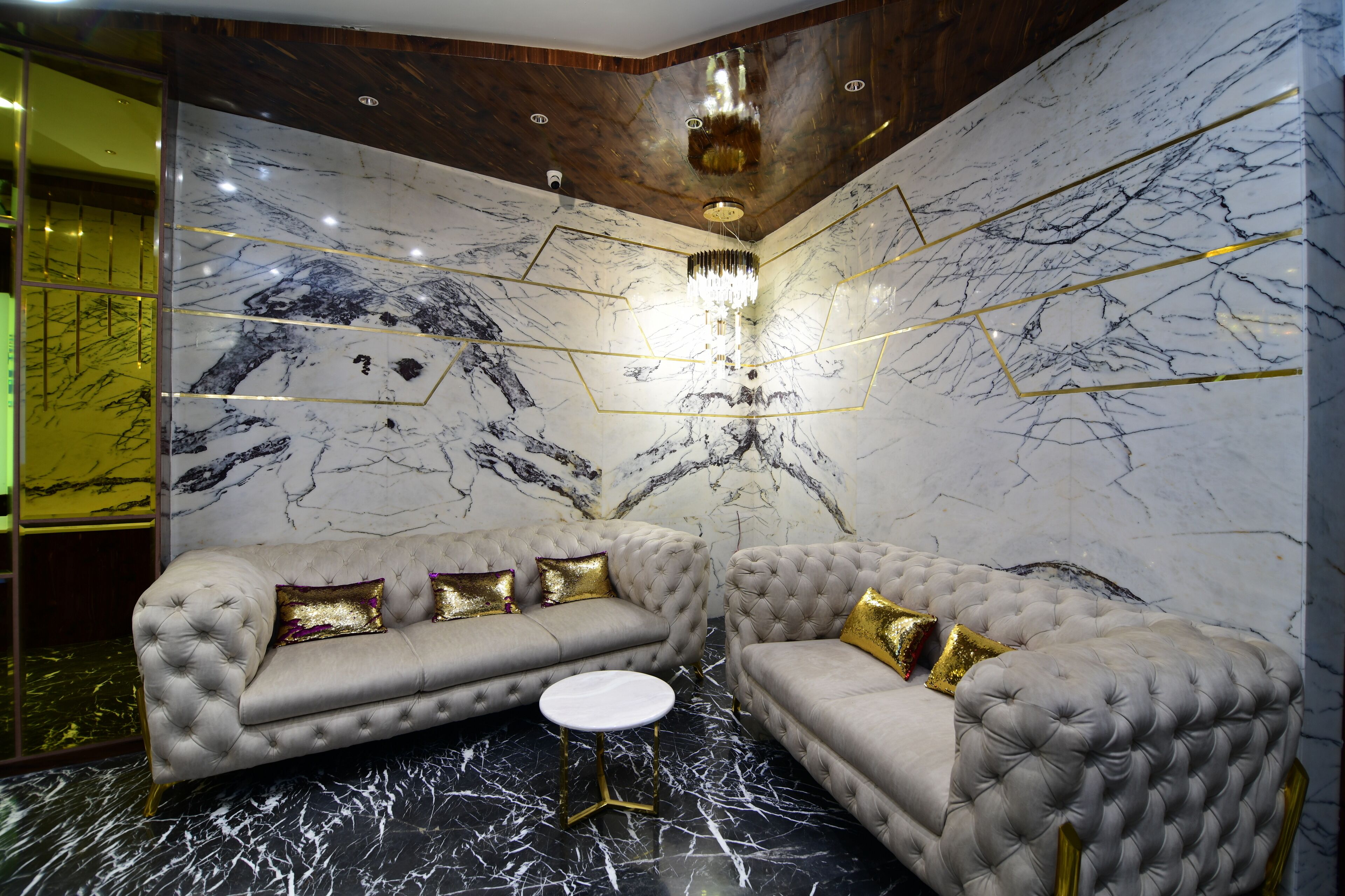 A luxurious room with a marble wall, two tufted sofas, a round table, and a chandelier.