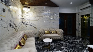 A luxurious room with a marble floor, a tufted sofa, a round table, and a chandelier. - Hotel Om Stay Well (Indore)