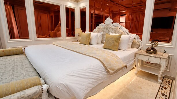 A spacious bedroom with a large bed, a nightstand, and a mirror. - Hotel Om Stay Well (Indore)