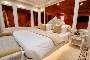 A spacious bedroom with a large bed, a nightstand, and a mirror. - Hotel Om Stay Well (Indore)