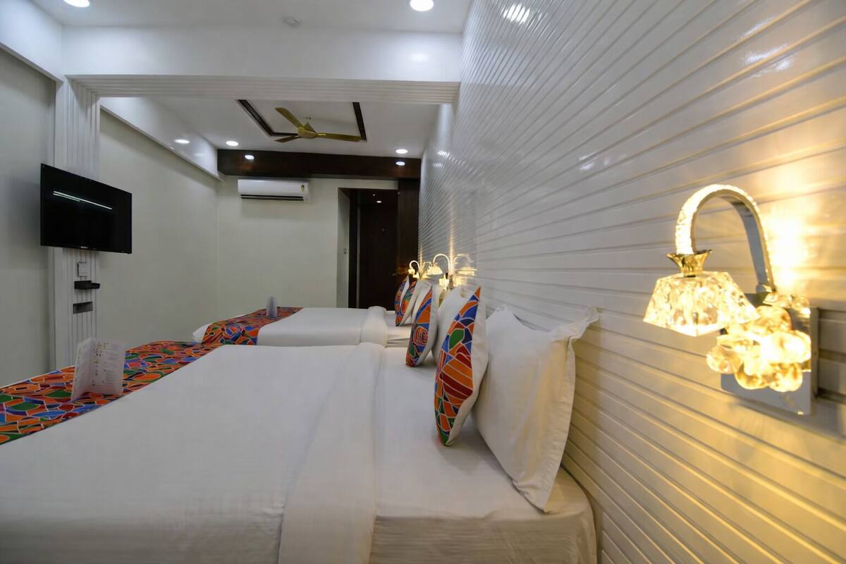 A hotel room with two beds, a flat-screen TV, a ceiling fan, and a wall-mounted light fixture.