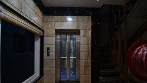 An elevator with a glass door, a marble wall, and a red circular decoration on the right. - Hotel Om Stay Well (Indore)