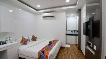 Habitación de hotel con cama, mesita de noche, aire acondicionado, televisor y una zona de kitchenette.