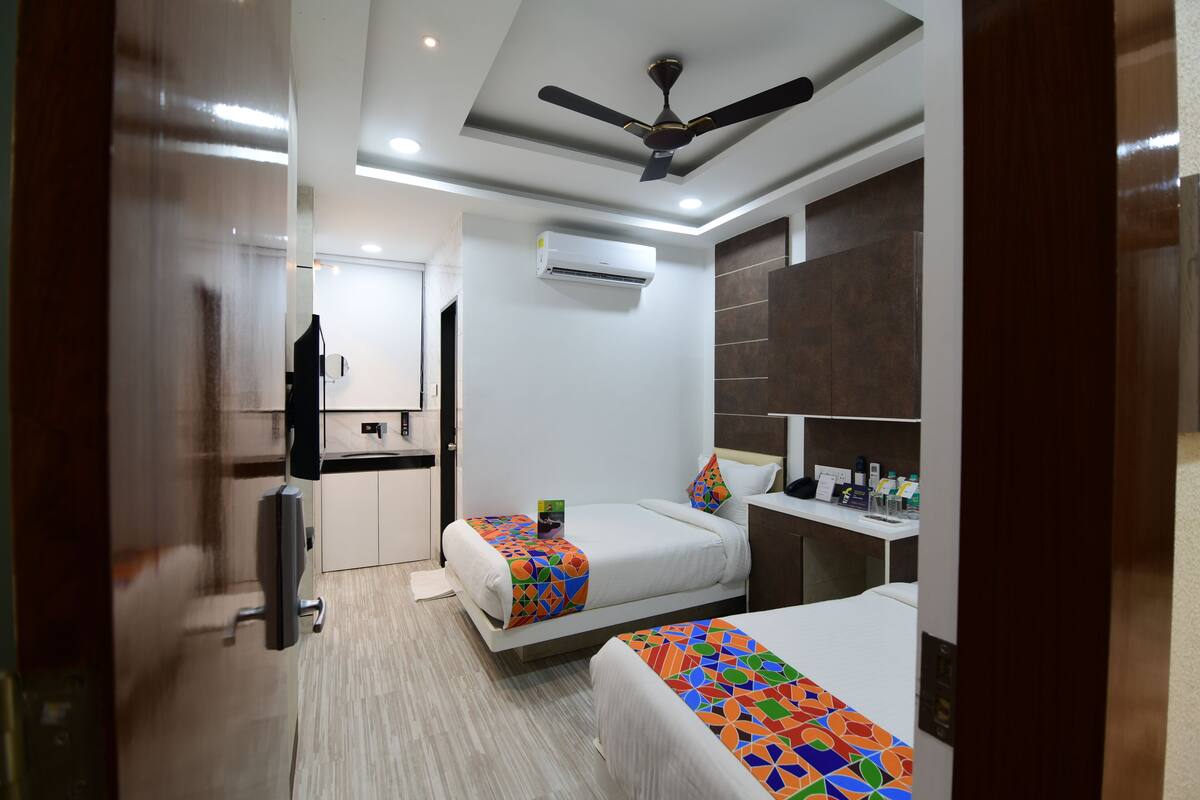 A modern hotel room with two beds, a ceiling fan, an air conditioning unit, a small desk, and a mirror.