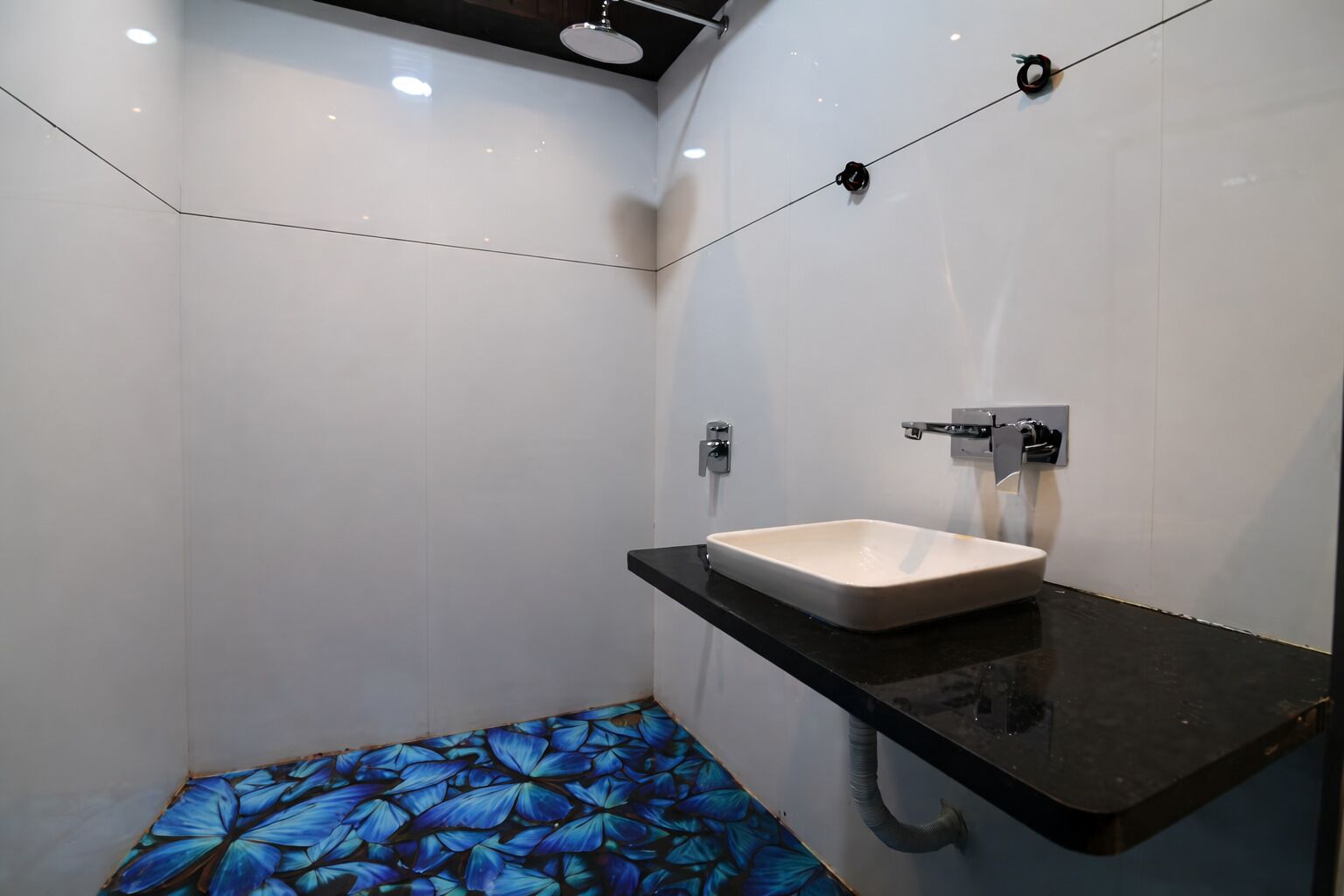 Une salle de bain avec un lavabo blanc, un plan de toilette noir et un sol orné d’un motif de papillons bleus.