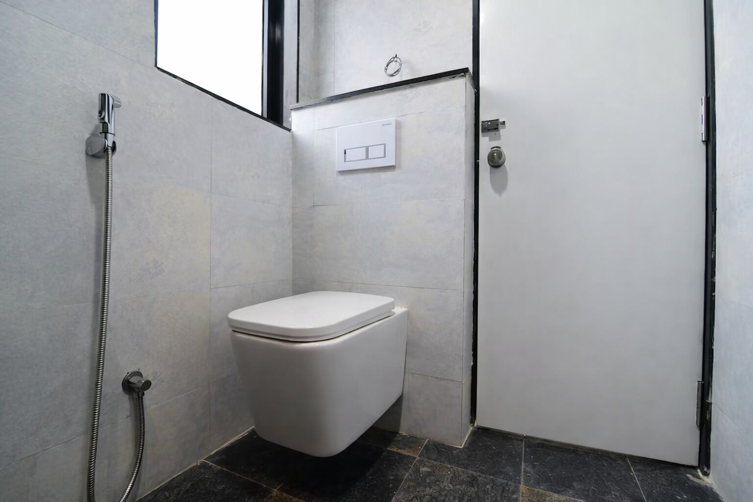 A small, modern bathroom with a white toilet, a shower, and a door with a handle.