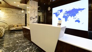 A reception area with a marble floor, a sofa, a reception desk, and a world map projection on the wall. - Hotel Om Stay Well (Indore)