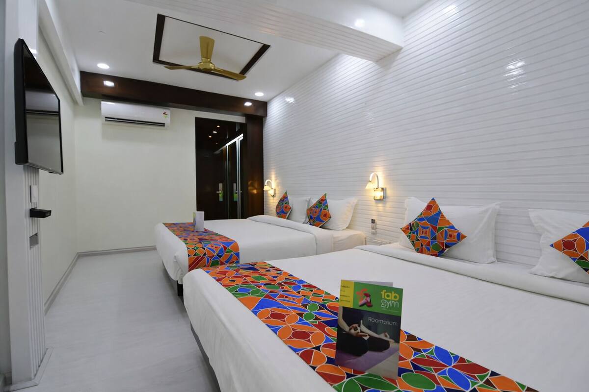 A hotel room with two beds, a TV, a ceiling fan, and a wall-mounted light fixture.