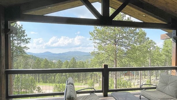 Een overdekt terras met uitzicht op een bos en bergen.