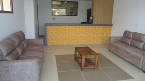 Ein Wohnzimmer mit zwei Sofas, einem Holztisch und einer Küchenzeile mit gelber Akzentwand.