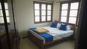Ein Schlafzimmer mit einem hölzernen Bett, zwei vergitterten Fenstern und einer Tür.