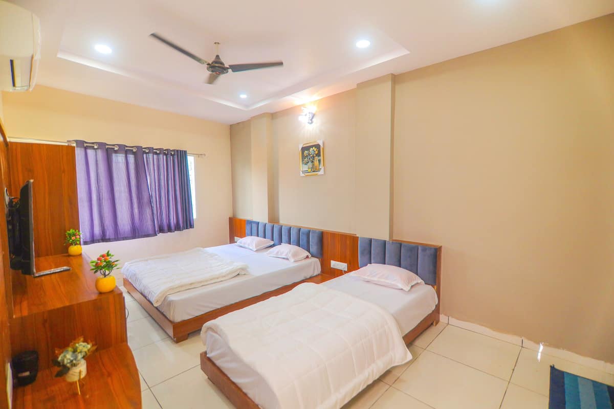 A hotel room with two beds, a ceiling fan, a TV, and a window with curtains.