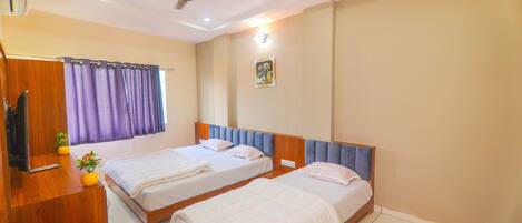A hotel room with two beds, a ceiling fan, a TV, and a window with curtains.