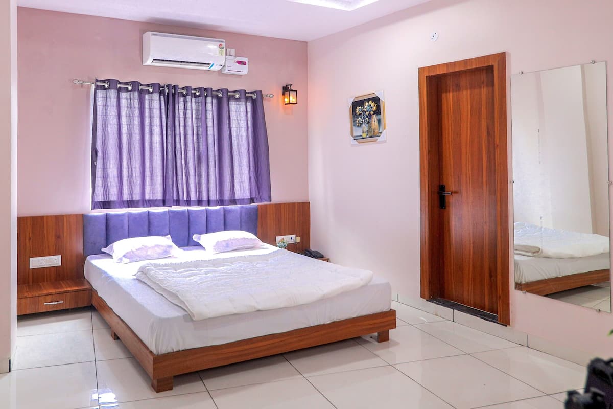 A bedroom with a wooden bed, a nightstand, a wall-mounted air conditioner, a door, and a mirror.