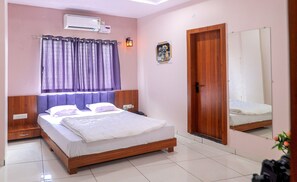 A bedroom with a wooden bed, a nightstand, a wall-mounted air conditioner, a door, and a mirror. - Hotel Dev Krishna Palace (Ujjain)