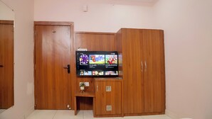 A room with a wooden wardrobe, a small cabinet, and a television mounted on the wall displaying various channels. - Hotel Dev Krishna Palace (Ujjain)