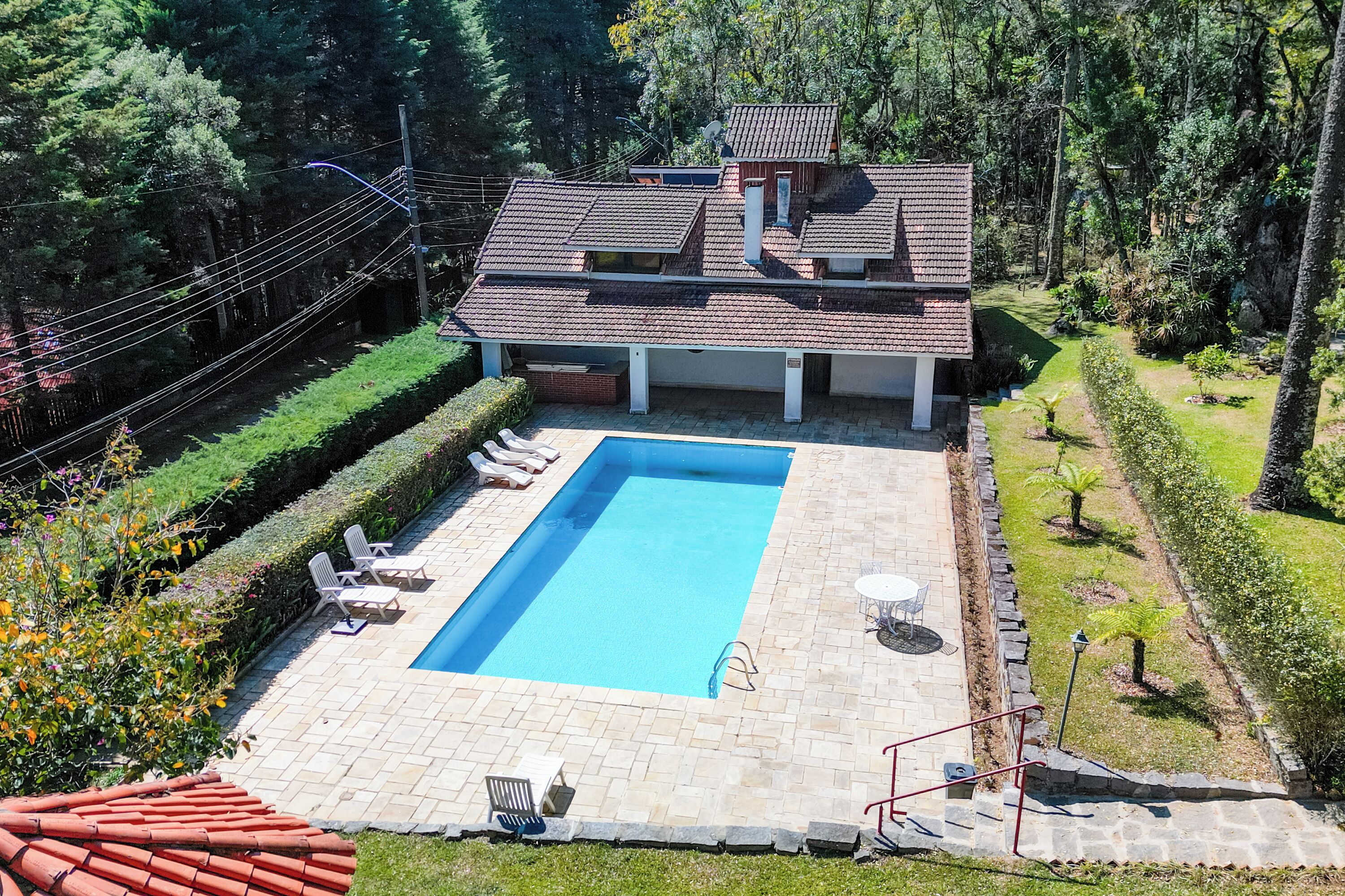 Une maison à deux étages avec une piscine rectangulaire, entourée d’une terrasse dallée et de chaises longues.