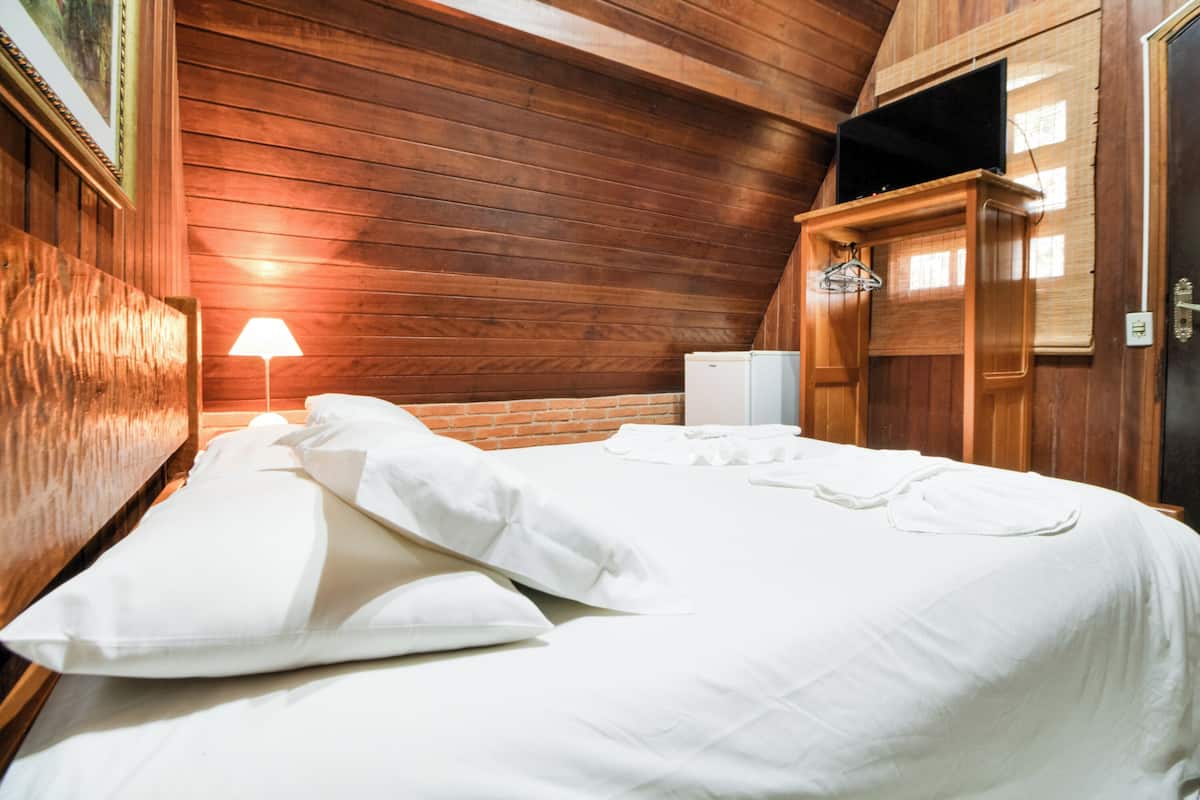 Une pièce aux murs lambrés, avec un lit, une lampe et un téléviseur fixé au mur.